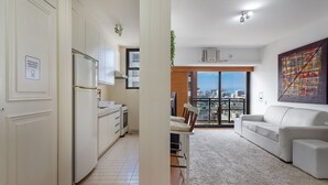A modern apartment with a kitchen, dining area, and a living room with a large window offering a city view. - (1008) Apartamento com 1 Quarto e Vista para o Cristo (Rio de Janeiro)