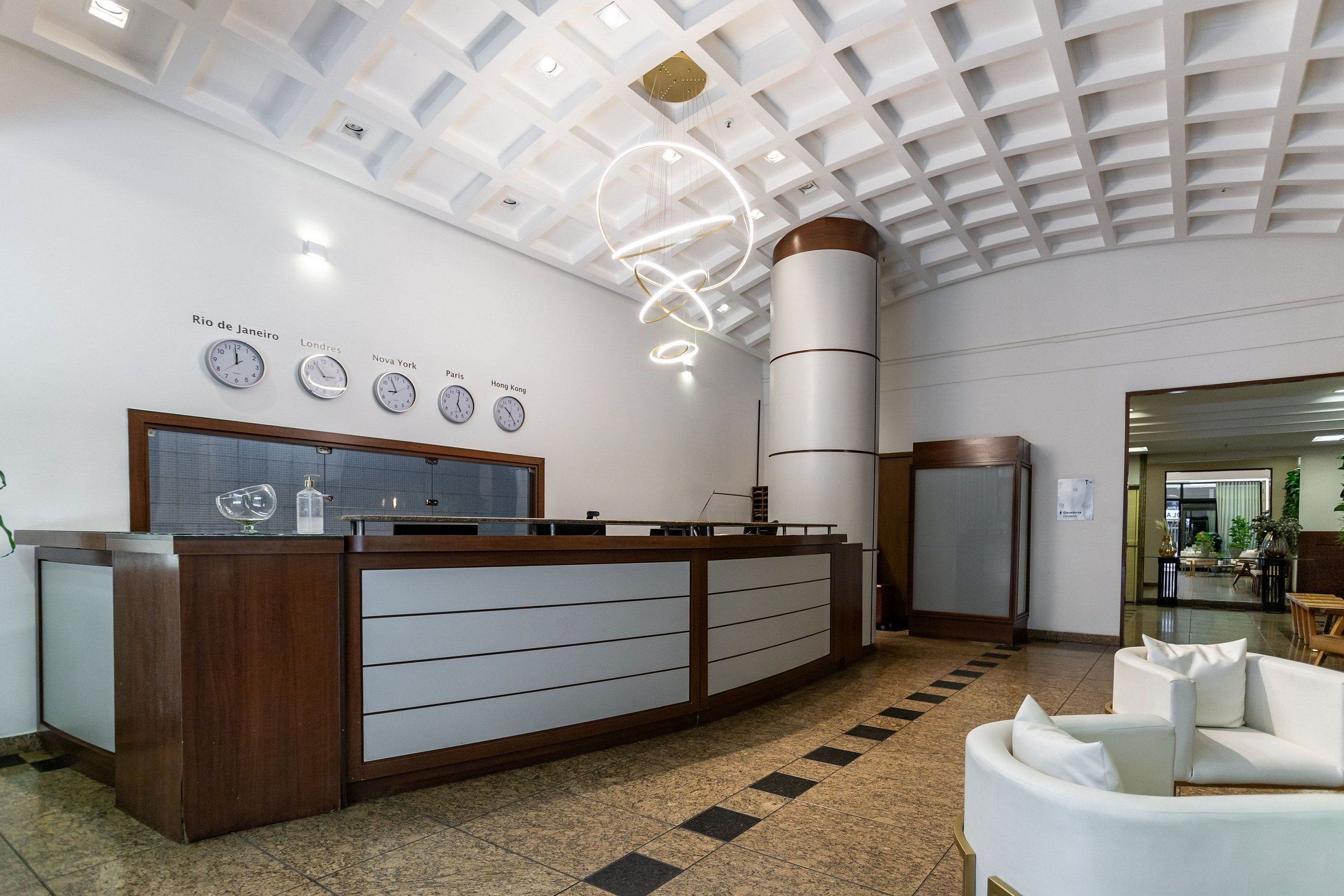 Uma receção com design moderno, teto com padrão geométrico e relógios a indicar a hora em diversas cidades.