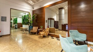 A lobby with a checkered floor, wooden walls, and a large mirror reflecting the space. There are several chairs and a table, along with potted plants. - (1008) Apartamento com 1 Quarto e Vista para o Cristo (Rio de Janeiro)