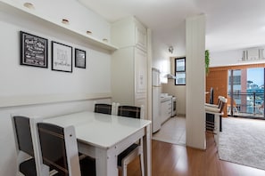 A modern kitchen with white cabinets, a dining table with chairs, and a view of the city through large windows. - (1008) Apartamento com 1 Quarto e Vista para o Cristo (Rio de Janeiro)