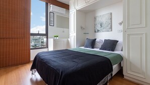 A bedroom with a large bed, a city view, white walls, and a window with blinds. - (1008) Apartamento com 1 Quarto e Vista para o Cristo (Rio de Janeiro)