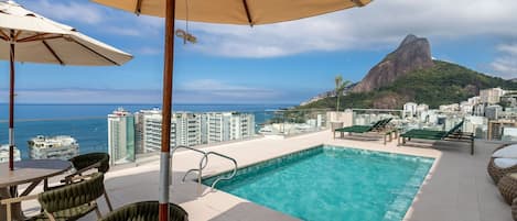 A rooftop pool with a view of a city and a mountain.
