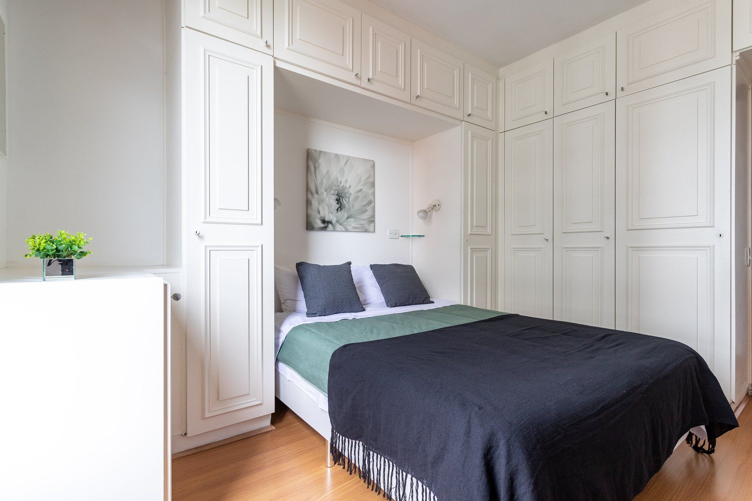A bedroom with a bed, a nightstand, a potted plant, and a wardrobe.