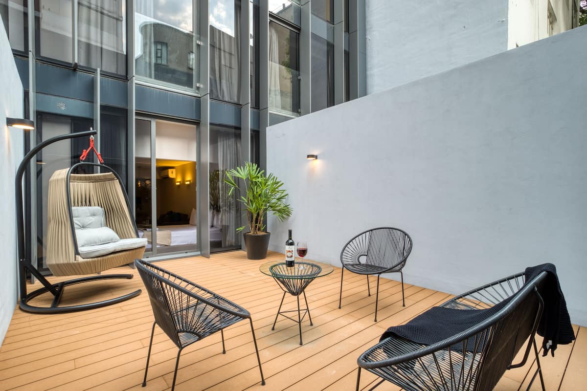 A modern outdoor seating area with a wooden deck, a hanging chair, and two metal chairs.