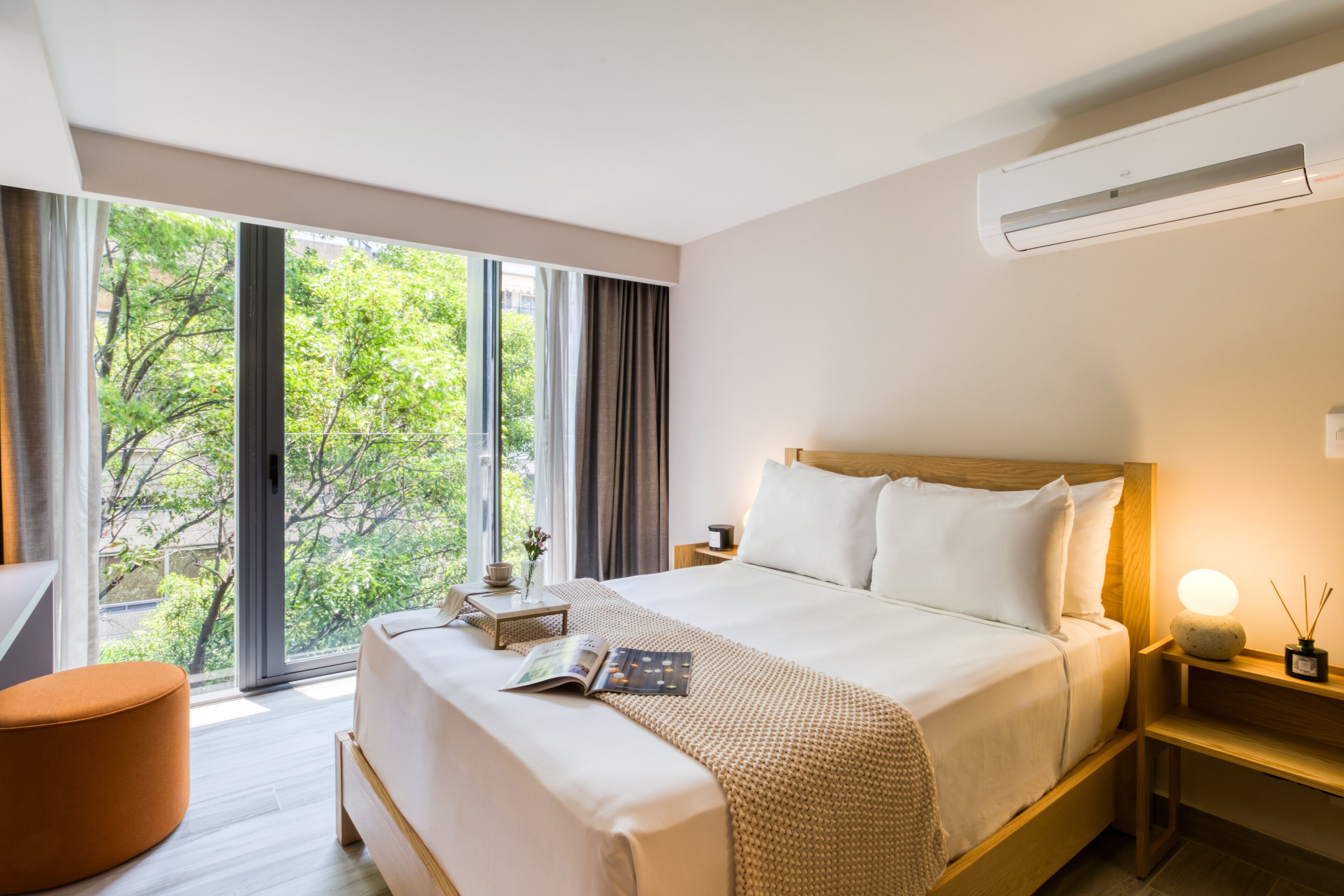 Habitación de hotel moderna con una cama grande, una mesita de noche con lámpara, una ventana con cortinas y vistas a zonas verdes.
