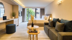 A modern hotel room with a sofa, a desk, and a bed. There is a window with a view of buildings and trees. - ULIV Parque Lincoln (Mexico City)