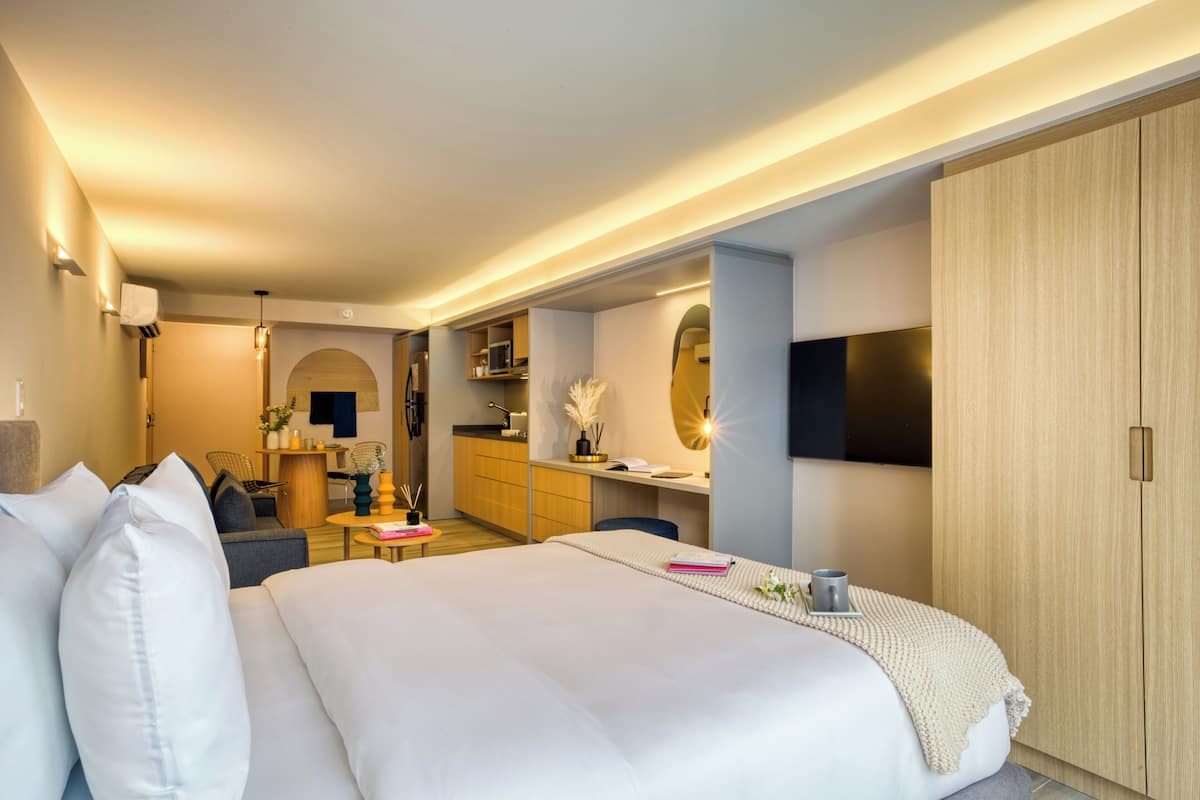 A modern hotel room with a large bed, a desk, a TV, and a wardrobe.