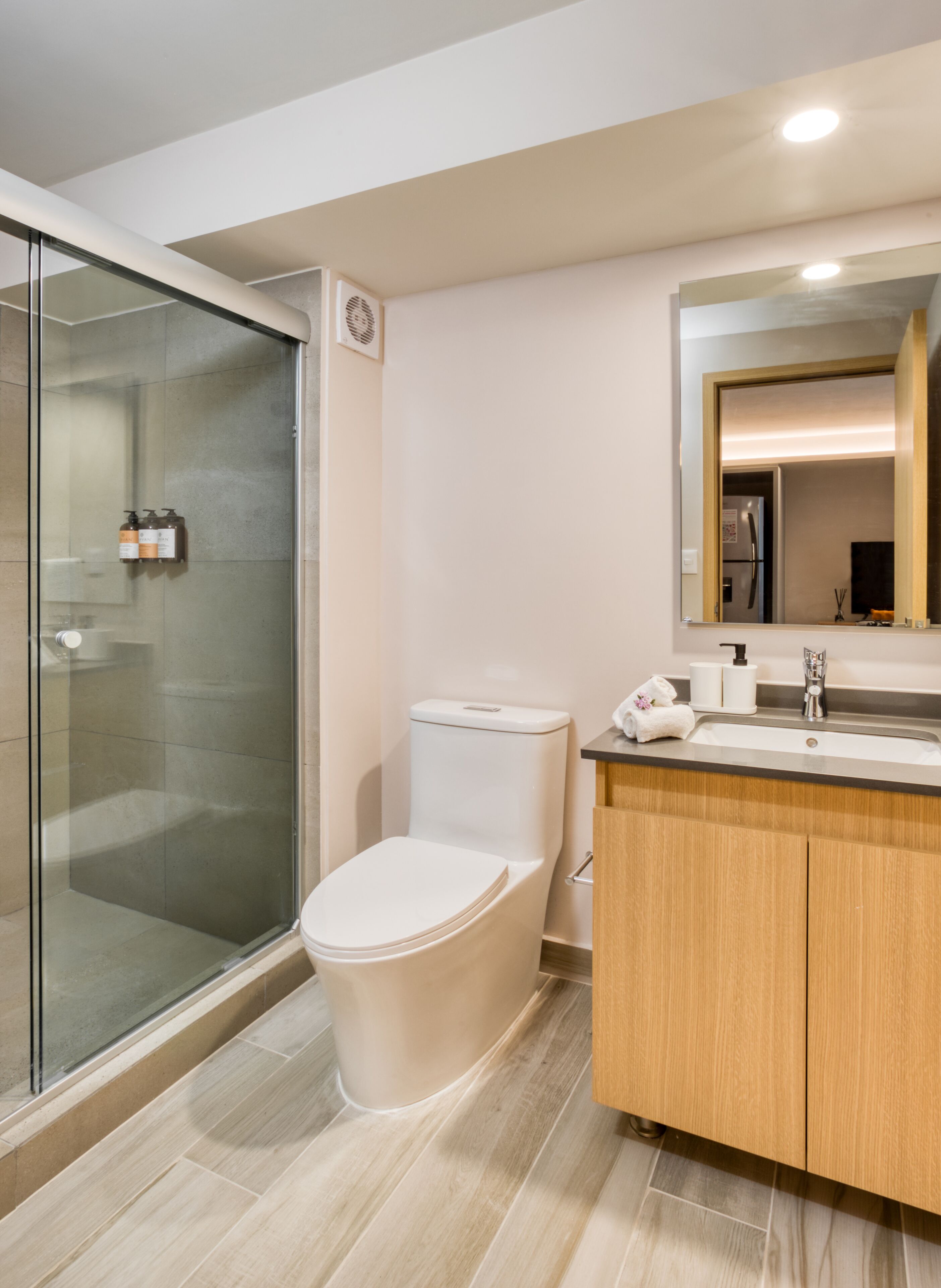 A modern bathroom with a glass shower enclosure, a toilet, a wooden vanity with a mirror, and a sink.