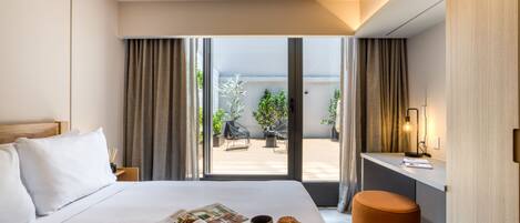 Una habitación de hotel con una cama, una bandeja de desayuno con un muffin y café, un escritorio con una lámpara, y vistas del patio exterior.