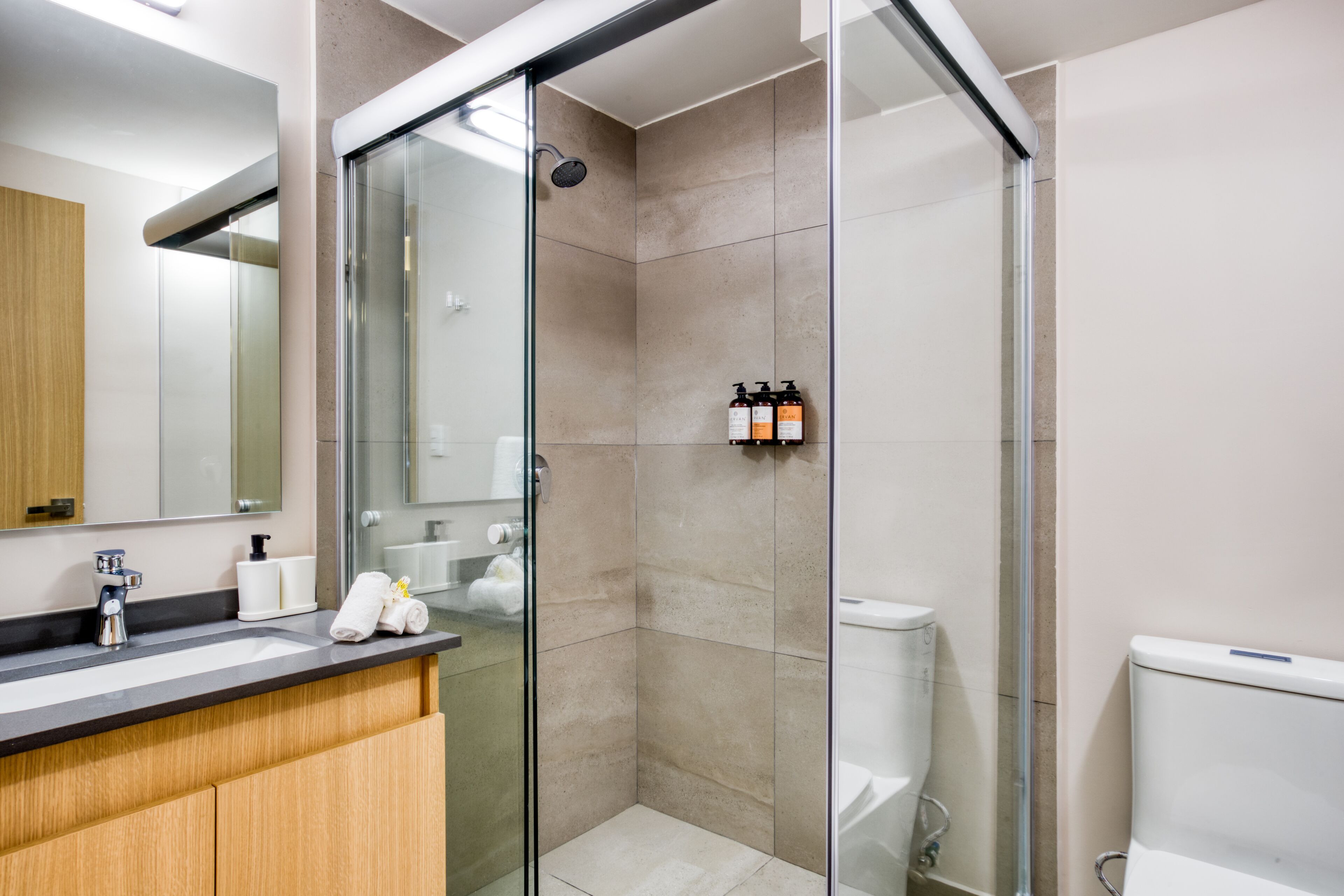 Un baño moderno con cabina de ducha de vidrio, un lavabo con artículos de aseo y un inodoro.