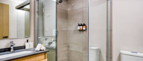 Un baño moderno con cabina de ducha de vidrio, un lavabo con artículos de aseo y un inodoro.