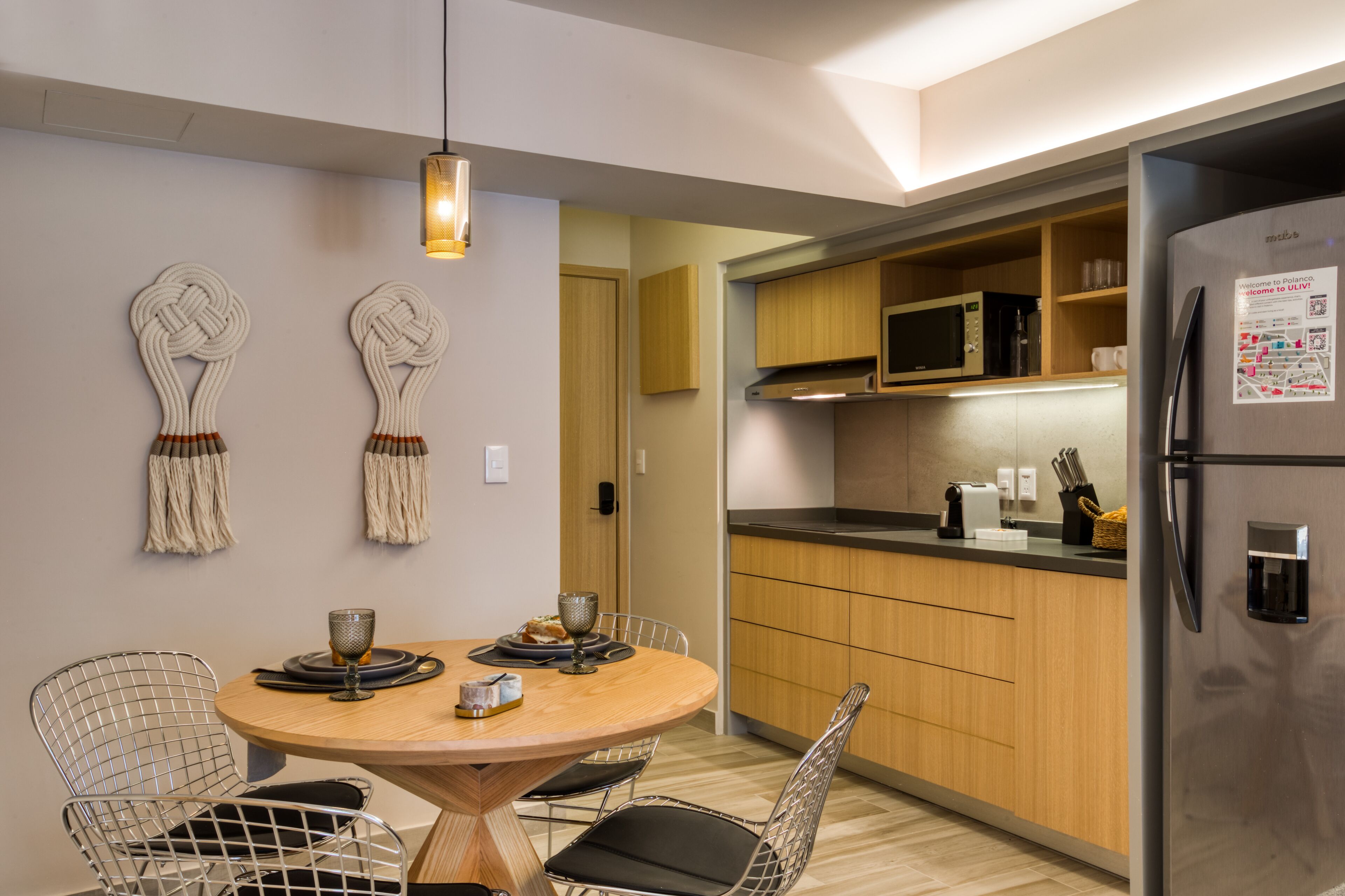 A modern kitchen with wooden cabinets, a stainless steel refrigerator, and a dining area with a round table and chairs.