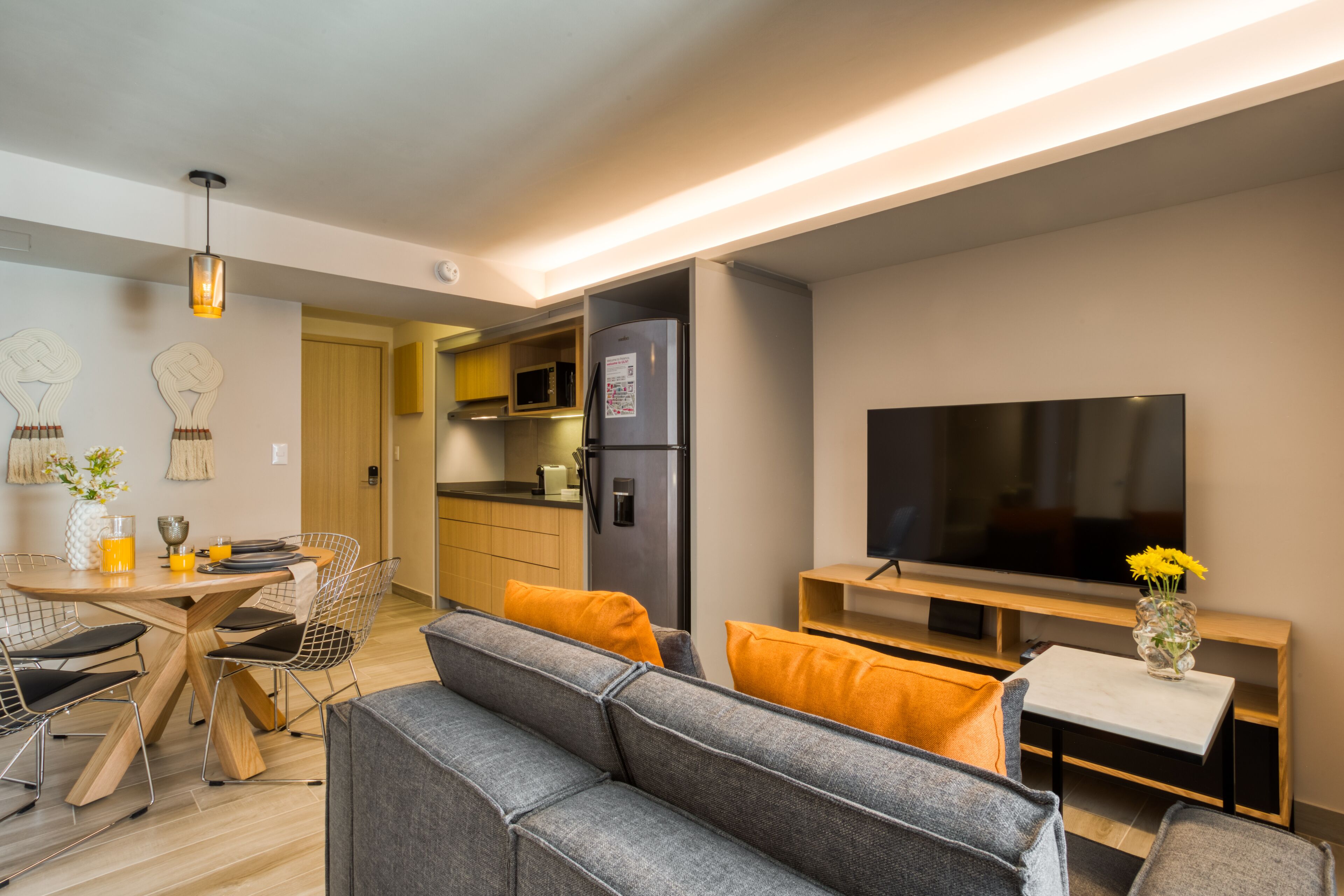 Uma sala de estar moderna com um sofá cinzento, uma televisão de tela plana e um espaço de jantar com uma mesa e cadeiras de madeira.