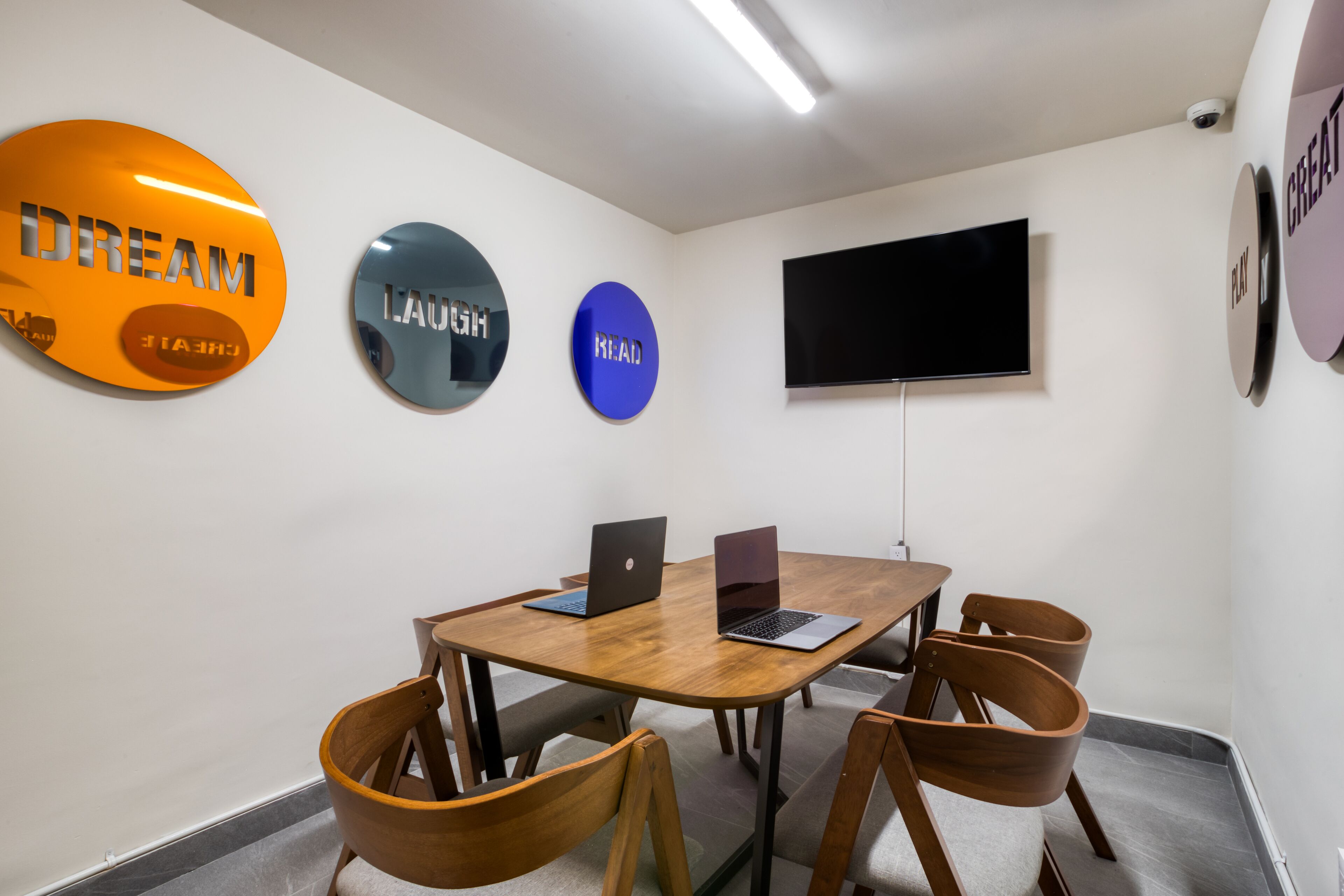 Un salón de conferencias con una mesa de madera, cuatro sillas de madera, dos ordenadores portátiles y tres adhesivos decorativos con mensajes motivadores.