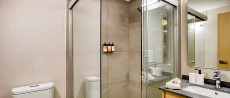 A modern bathroom with a glass-enclosed shower, a white toilet, a sink with a wooden vanity, and a mirror above the sink.