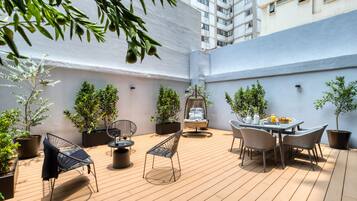 A rooftop patio with a wooden deck, outdoor seating, potted plants, and a hanging chair.