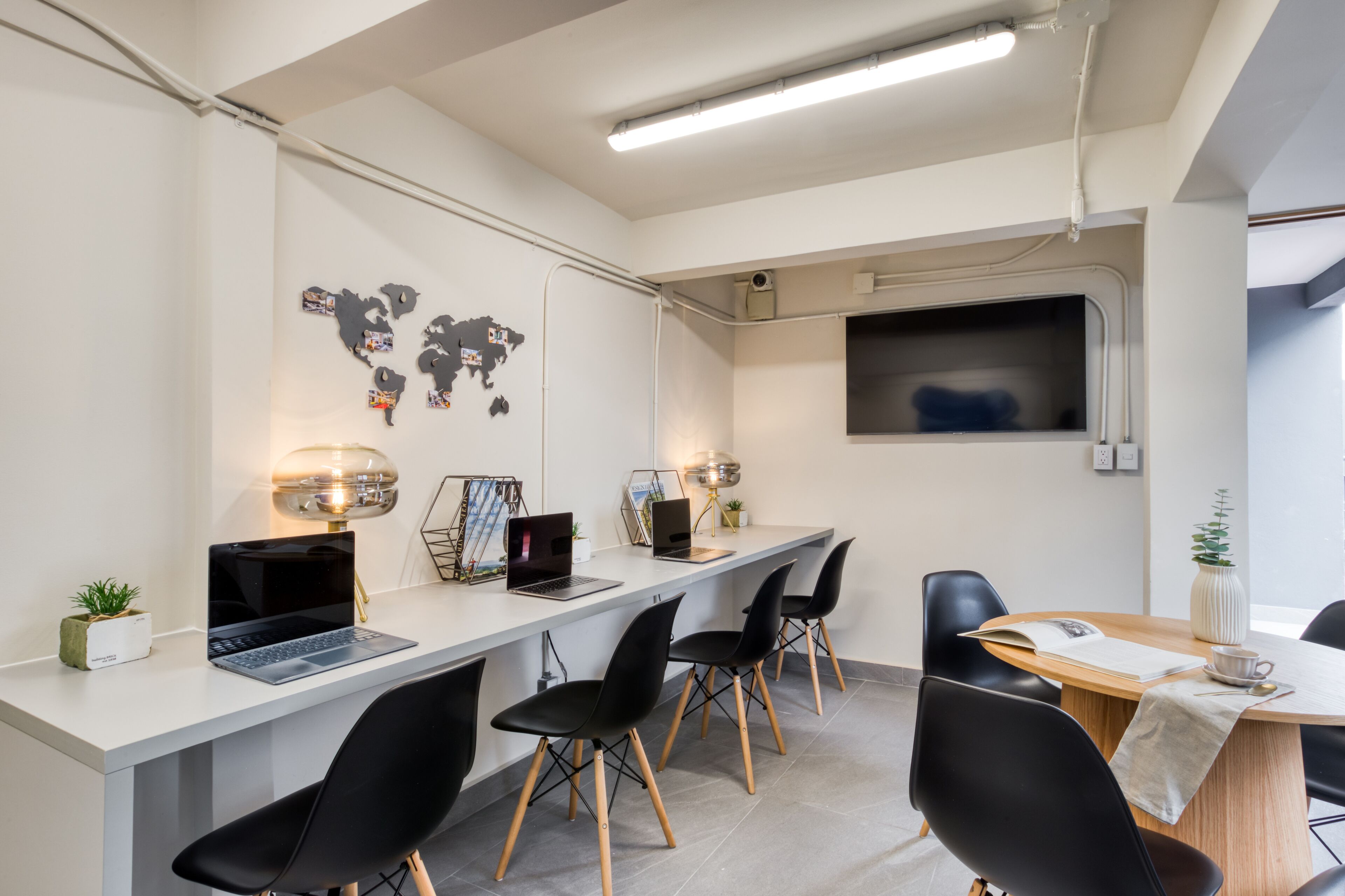 Un espace de bureau moderne avec un grand bureau blanc, plusieurs chaises noires et deux ordinateurs portables.