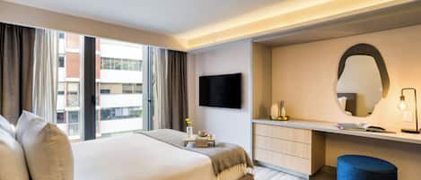 Habitación de hotel moderna con una cama grande, un escritorio, un espejo y vistas a la ciudad.