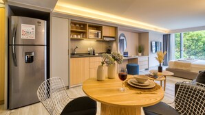 A modern kitchen with a built-in refrigerator, microwave, and oven. There is a dining area with a round wooden table, two chairs, and a glass of red wine. The kitchen has wooden cabinets and a window with a view of greenery outside. - ULIV Parque Lincoln (Mexico City)