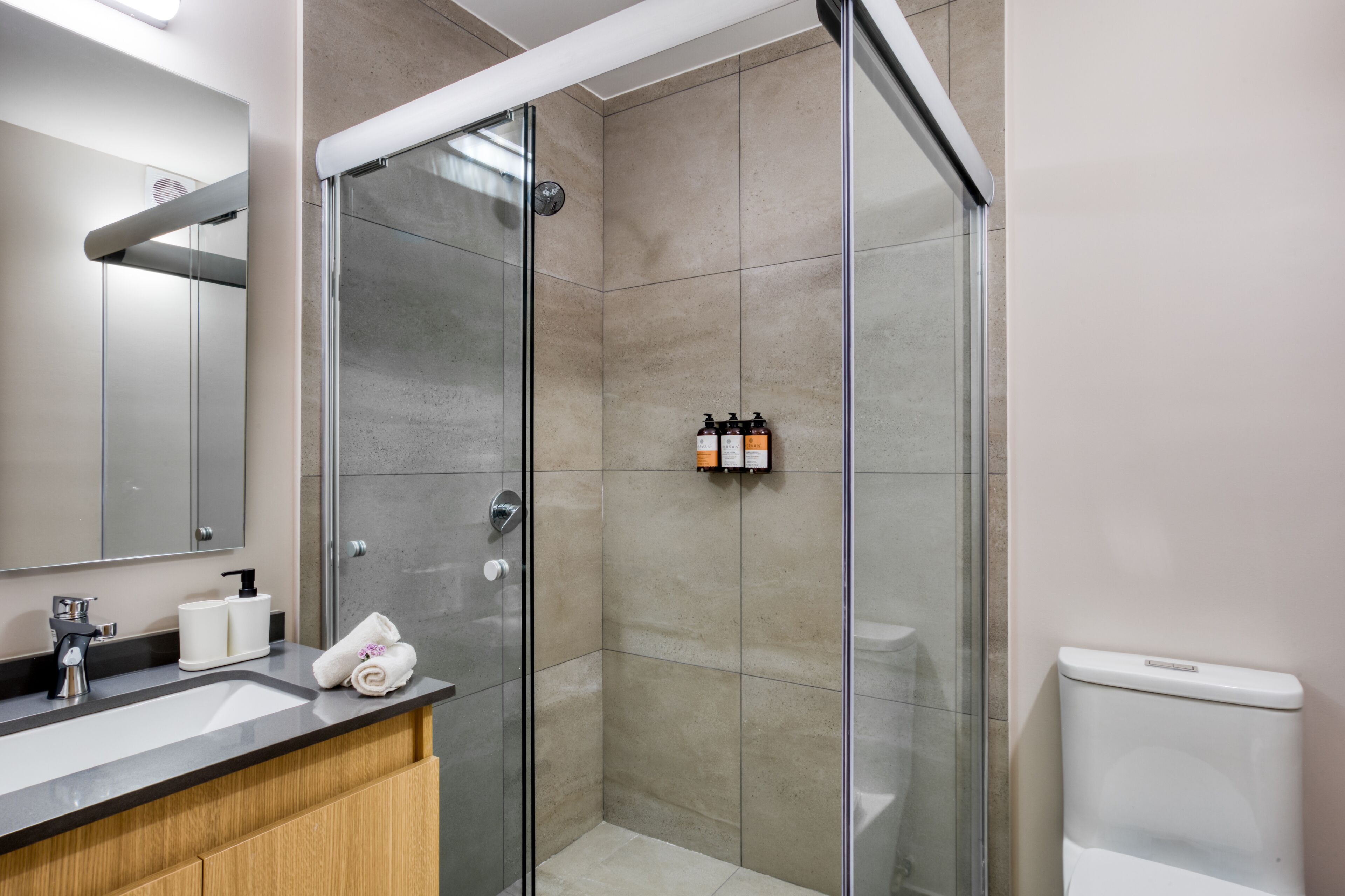 A modern bathroom with a glass shower enclosure, a sink with toiletries, and a toilet.
