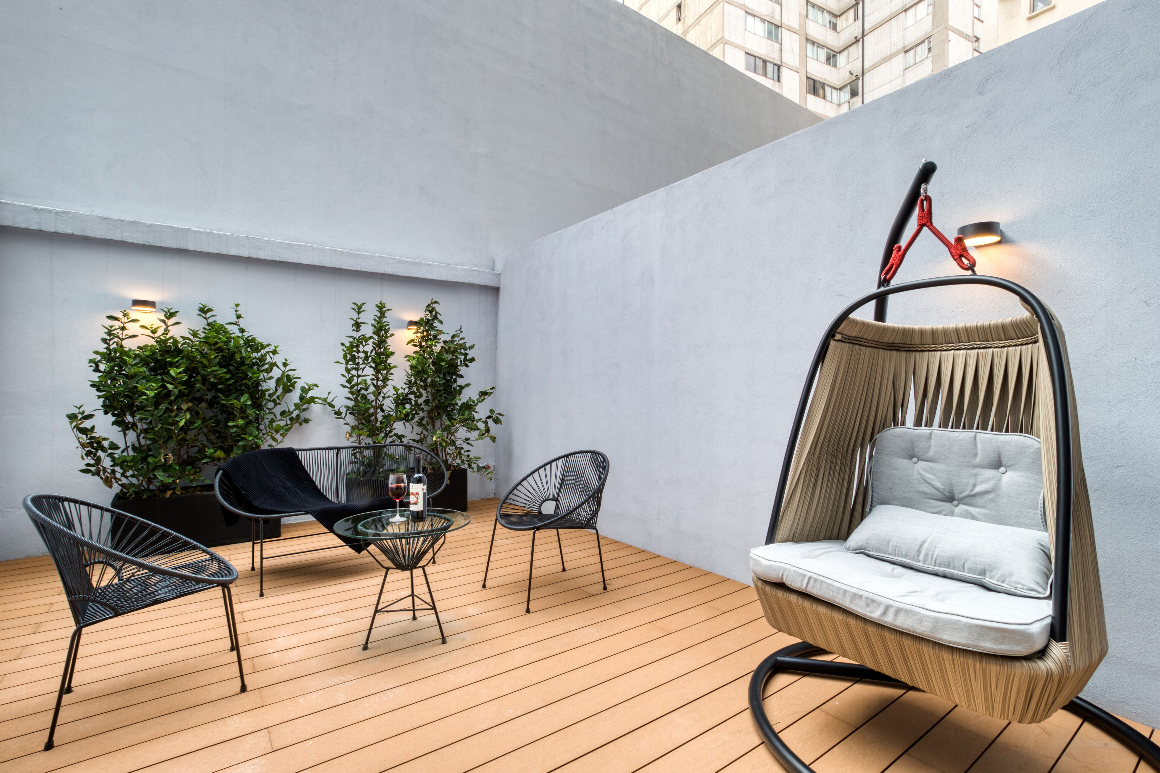 A modern outdoor seating area with a hanging chair, two lounge chairs, and a glass table.