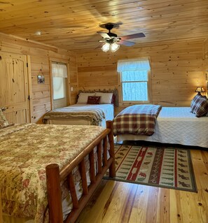 Une chambre confortable dans un chalet, avec deux lits, des murs en bois, un ventilateur de plafond et une fenêtre donnant sur la forêt.