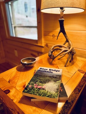 Una mesa de madera con un libro titulado 'Blue Ridge Folklife' de Ted Olson, una lámpara y un cuenco.