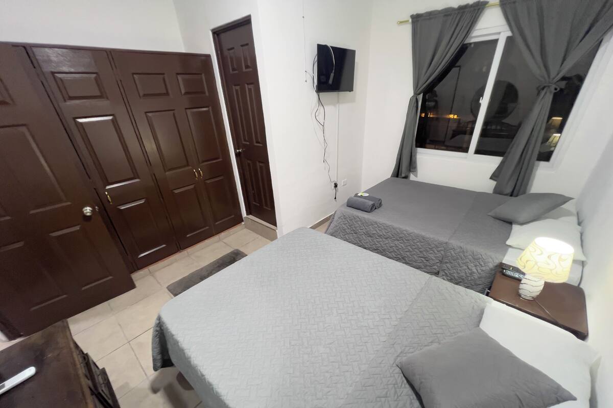 A bedroom with two beds, a TV mounted on the wall, and a window with curtains.