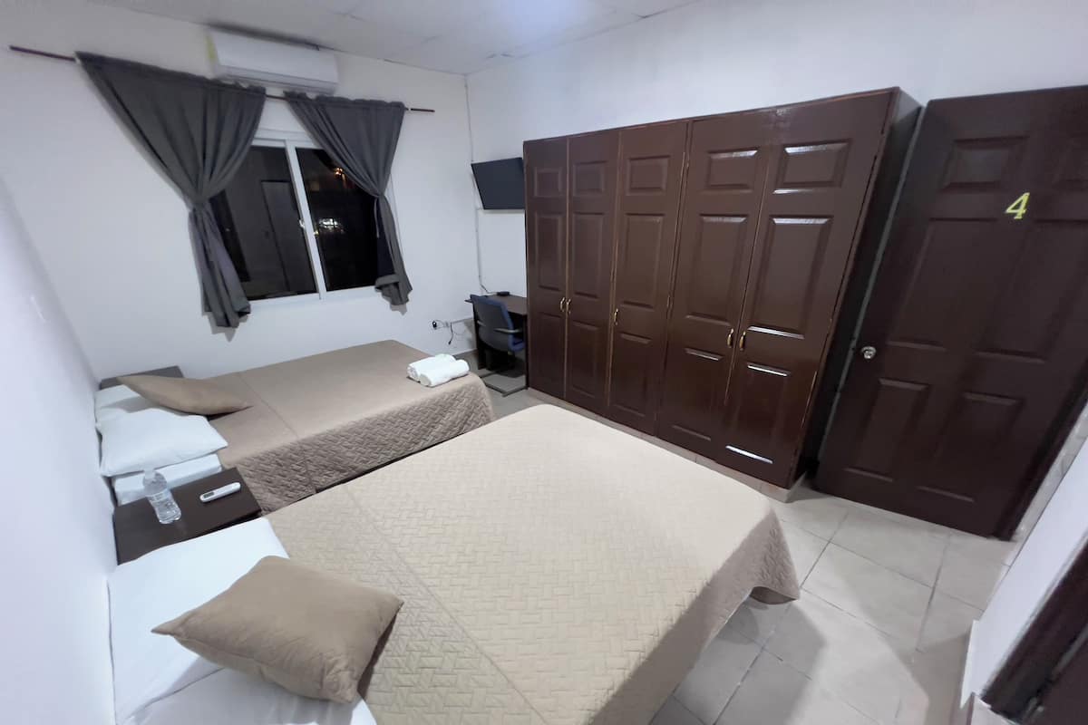 A hotel room with two beds, a wardrobe, a desk with a chair, and a window with curtains.