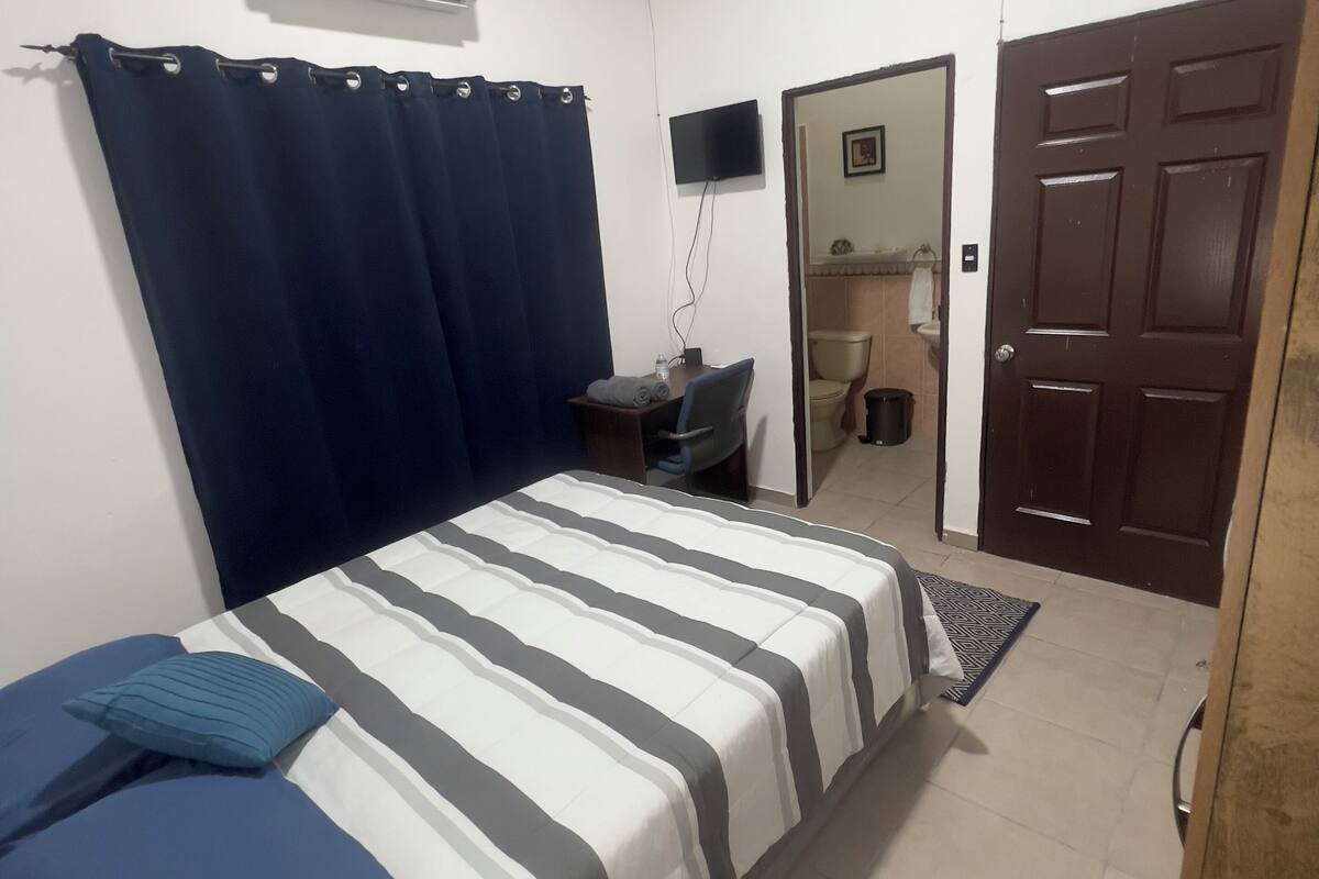 A bedroom with a bed, a TV, a door, and an air conditioning unit.