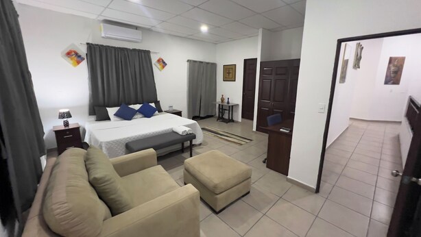 Una habitación de hotel con cama, sofá, otoman, escritorio y silla.