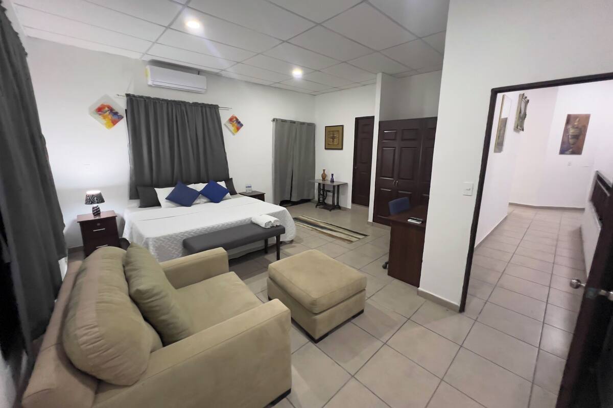 A hotel room with a bed, a sofa, an ottoman, a desk, and a chair.