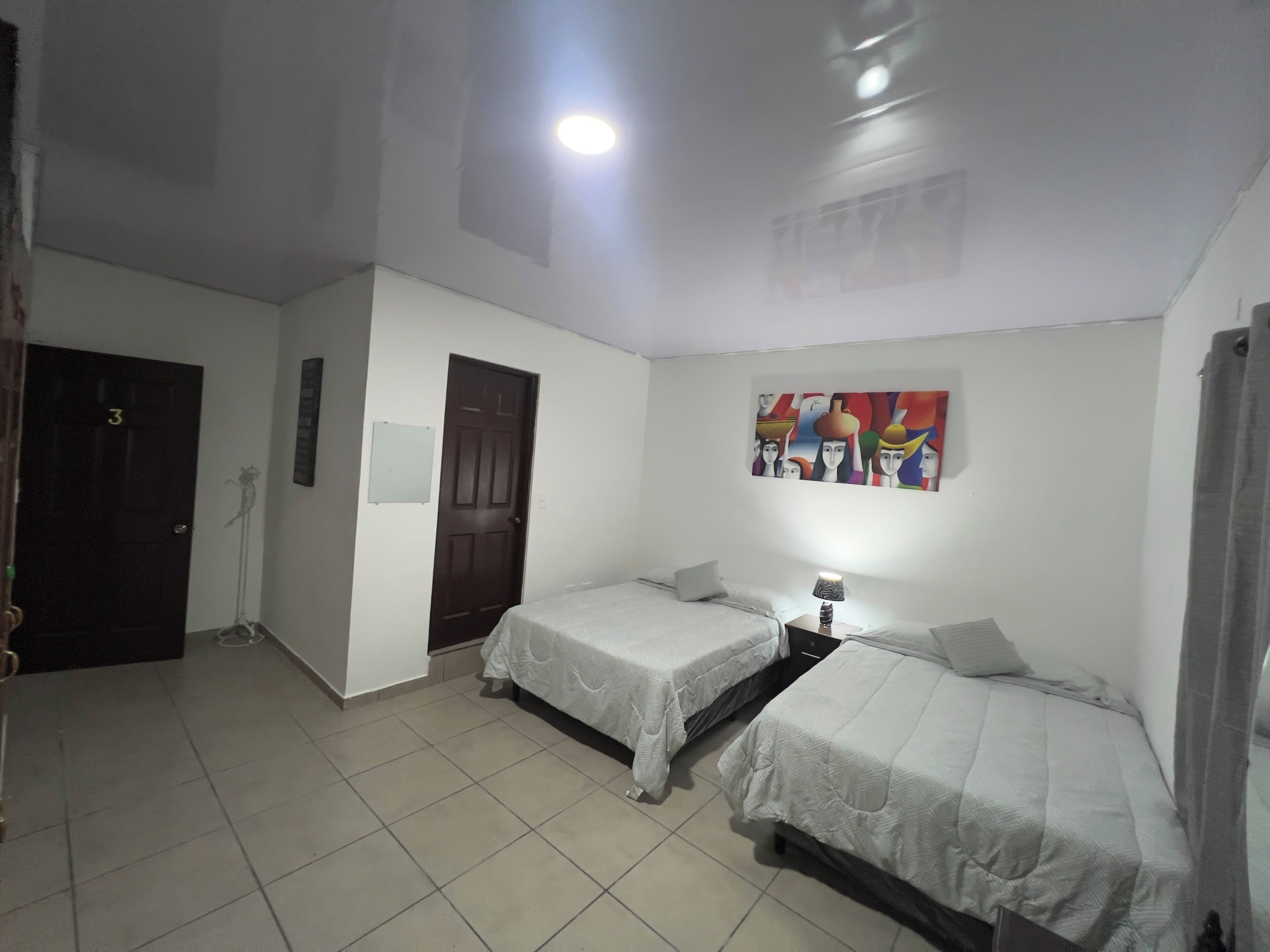 A room with two single beds, a door, a wall-mounted artwork, and a ceiling light.