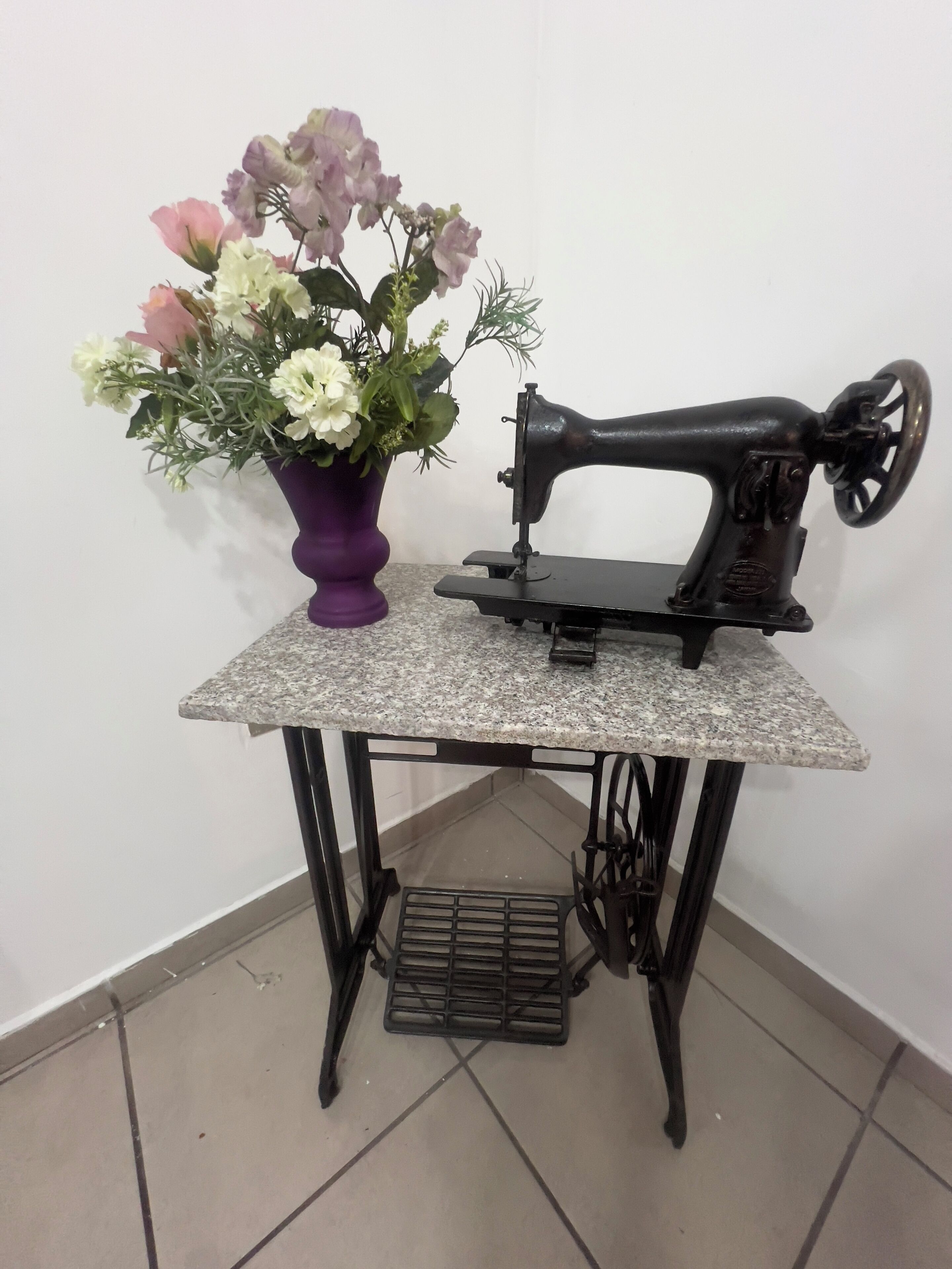 A vintage sewing machine on a small table with a potted plant beside it.