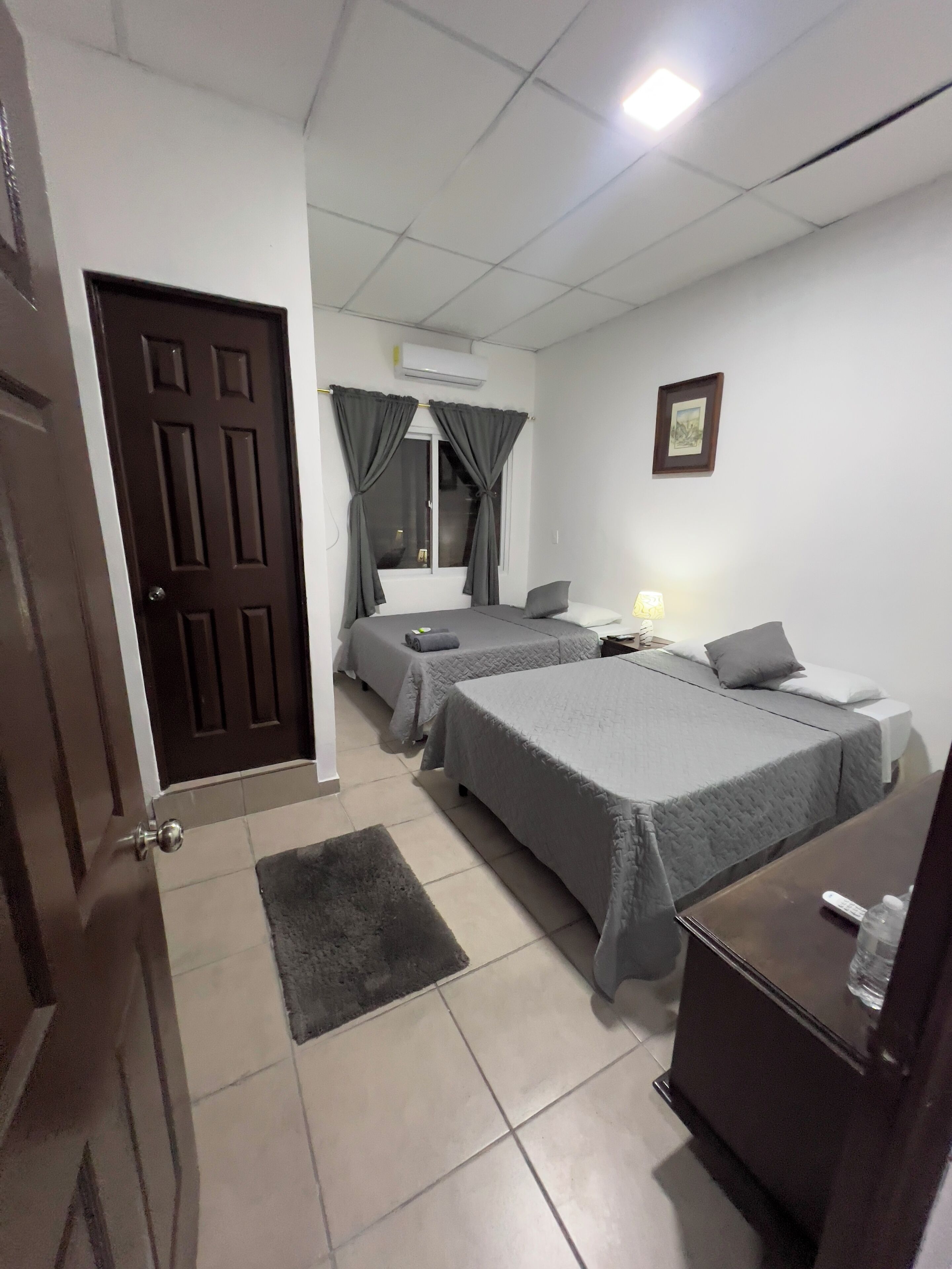 Een hotelkamer met twee bedden, een bureau, een stoel, een tafeltje, een lamp, een schilderij aan de muur en een deur.