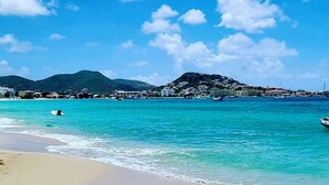 A beach with clear turquoise waters, a person swimming, and a mountainous backdrop.
