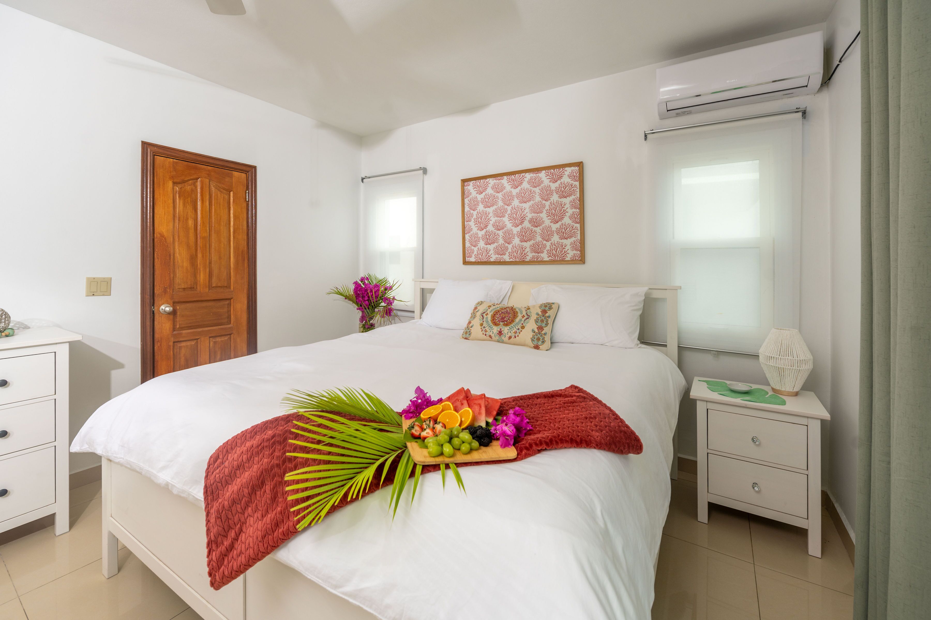 A neatly arranged bedroom with a bed, bedside tables, a wooden door, and a wall-mounted air conditioner.