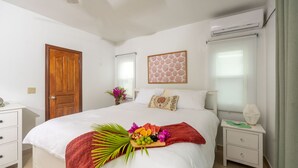 A neatly arranged bedroom with a bed, bedside tables, a wooden door, and a wall-mounted air conditioner.