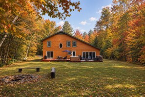 A wooden cabin with a deck, outdoor seating, and a fire pit in a forested area. - Spacious 4BR / 5 Bath Home - Hot Tub / Pool Table / Ample Private Outdoor Space! (Pittsfield)