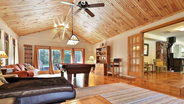 A spacious living room with a wooden ceiling, a pool table, leather sofas, and a view of the outdoors. - Spacious 4BR / 5 Bath Home - Hot Tub / Pool Table / Ample Private Outdoor Space! (Pittsfield)