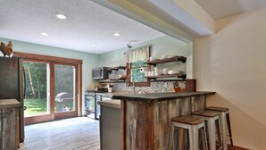 A modern kitchen with a bar area, wooden stools, and a view of the outdoors. - Spacious 4BR / 5 Bath Home - Hot Tub / Pool Table / Ample Private Outdoor Space! (Pittsfield)