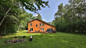 A wooden house with a deck, surrounded by a well-maintained lawn and trees. - Spacious 4BR / 5 Bath Home - Hot Tub / Pool Table / Ample Private Outdoor Space! (Pittsfield)