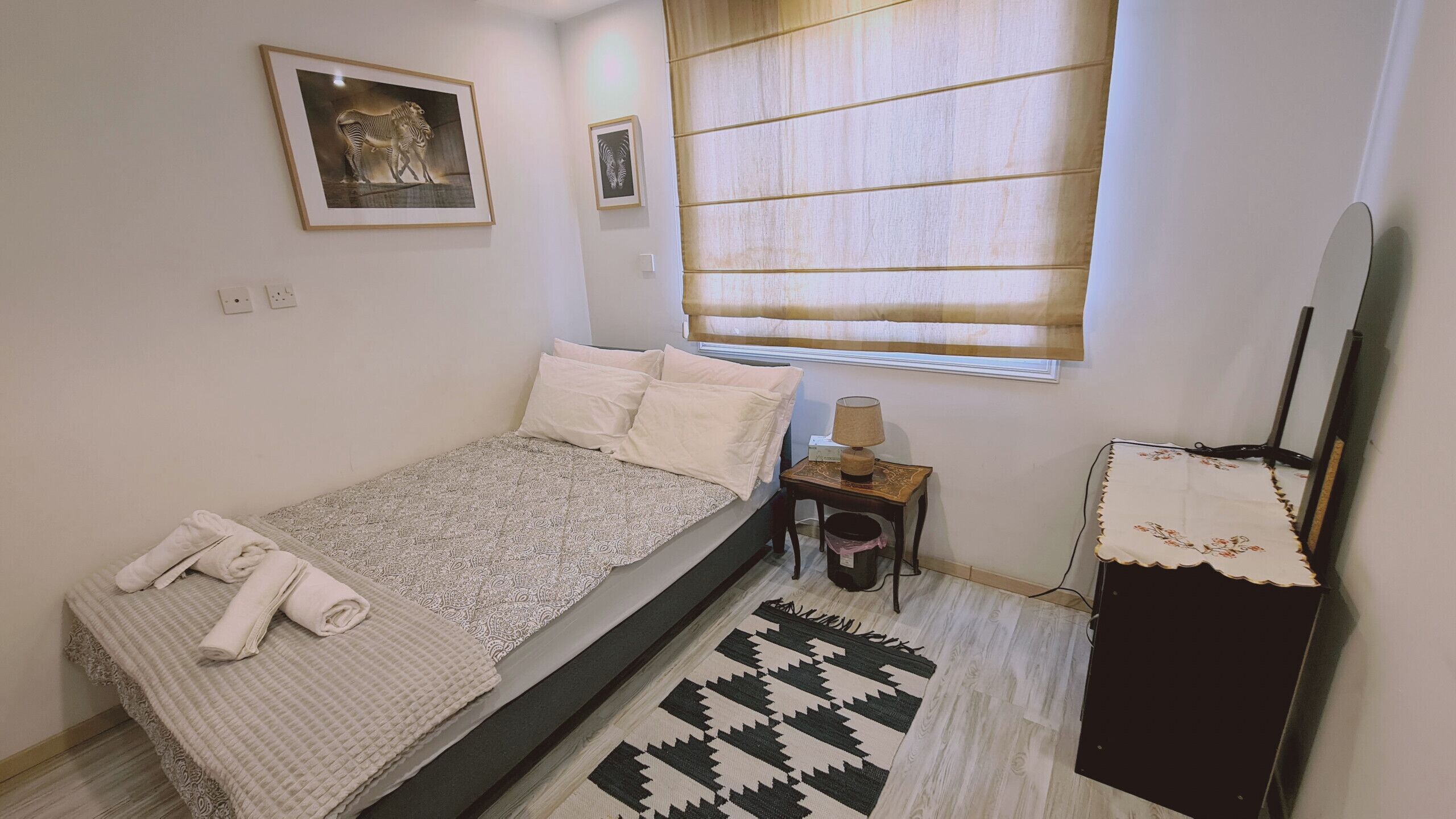 Une chambre à coucher avec un lit, des oreillers, une table de chevet avec une lampe, un tapis et un téléviseur fixé au mur.