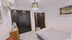 Un dormitorio con cama, armario, escritorio, lámpara colgante y un cuadro en la pared.