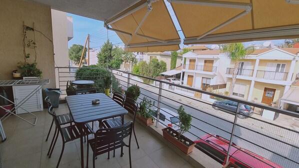 Un balcón con mesa y sillas, plantas en macetas y vistas a edificios residenciales.