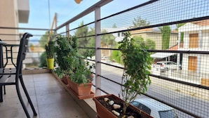 A balcony with potted plants, a chair, and a view of a street through a metal fence. - STAY Serenity Apartment (Engomi)