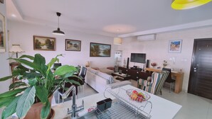 A modern living room with a dining area, featuring a large plant, a TV, and artwork on the walls. - STAY Serenity Apartment (Engomi)