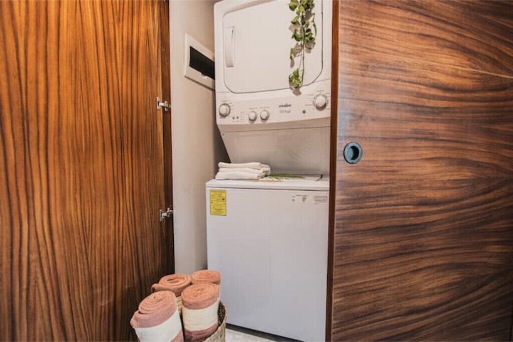 Een kleine wasruimte met een wasmachine en droger, een houten deur en netjes opgerolde handdoeken.