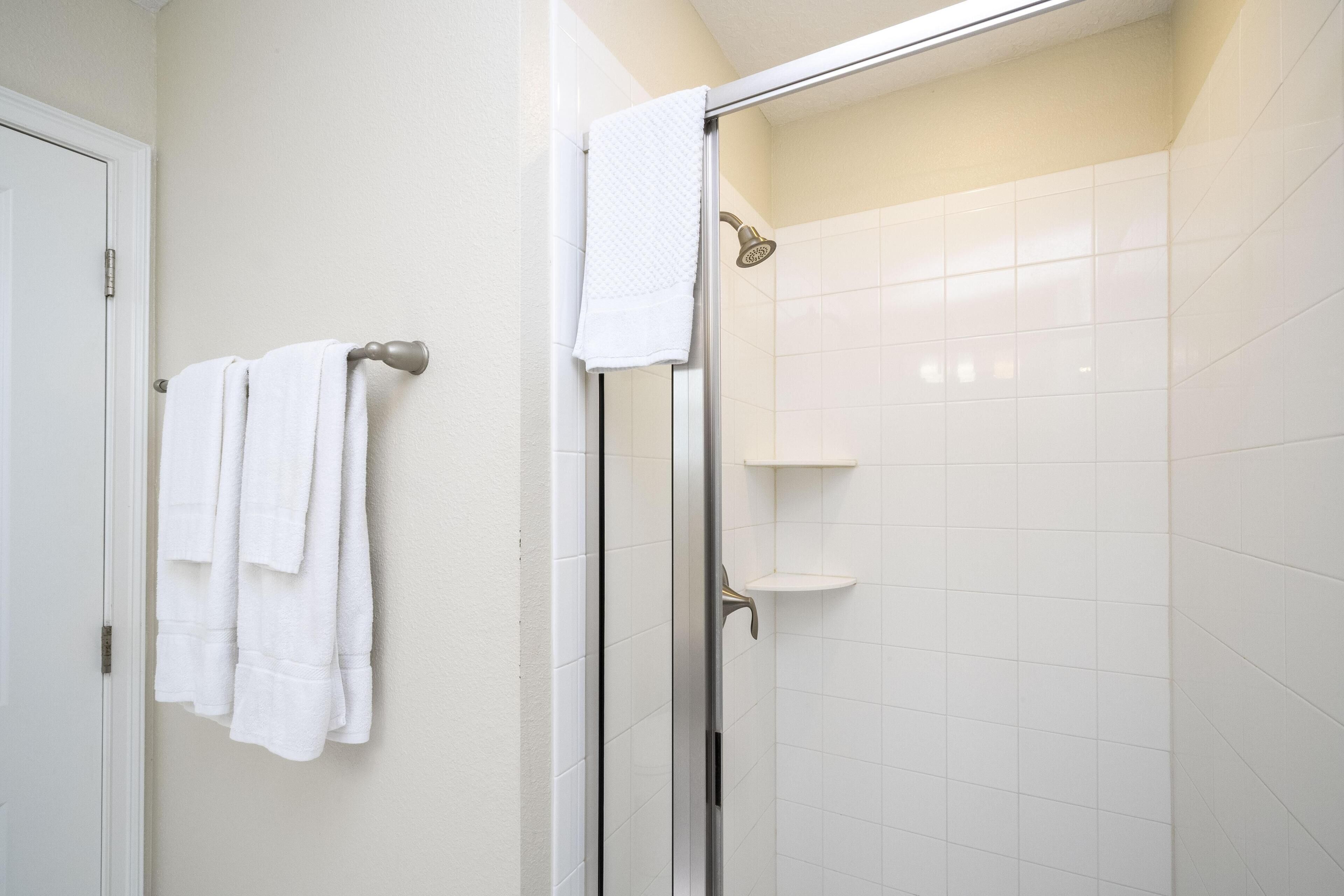 A bathroom with a glass shower enclosure, white tiled walls, and a towel rack with multiple towels.