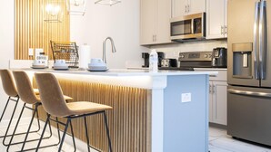 Une cuisine moderne dotée d’un îlot central, d’appareils électroménagers en acier inoxydable et d’un mur d’accent en bois.